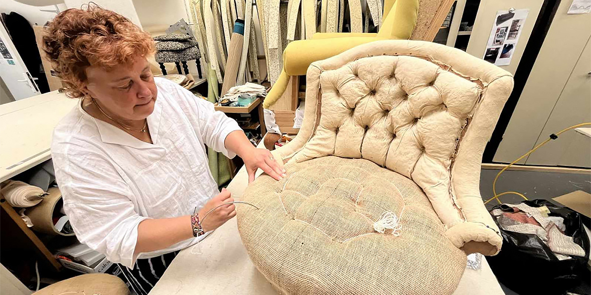 Hélène Navarre, experte internationale en tapisserie d’ameublement, posant dans son atelier avec une chaise en cours de restauration.