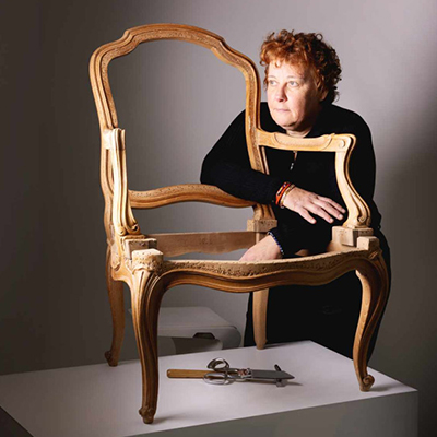 Hélène Navarre, experte internationale en tapisserie d’ameublement avec une chaise ancienne en cours de restauration.